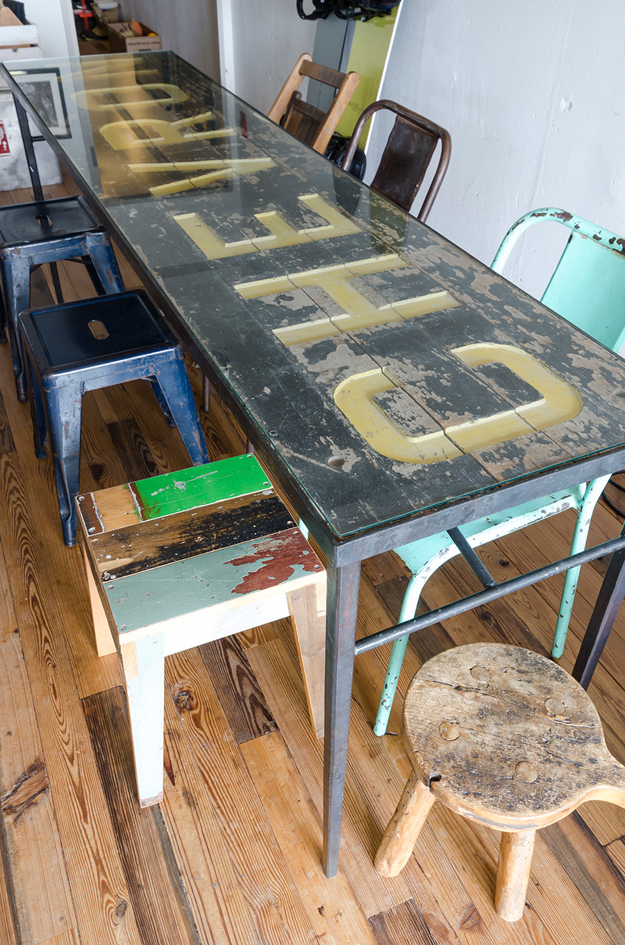 アイアンの骨に古い看板、ガラスの天板を載せたダイニングテーブル。手前のイスはオランダ人作家のもの。