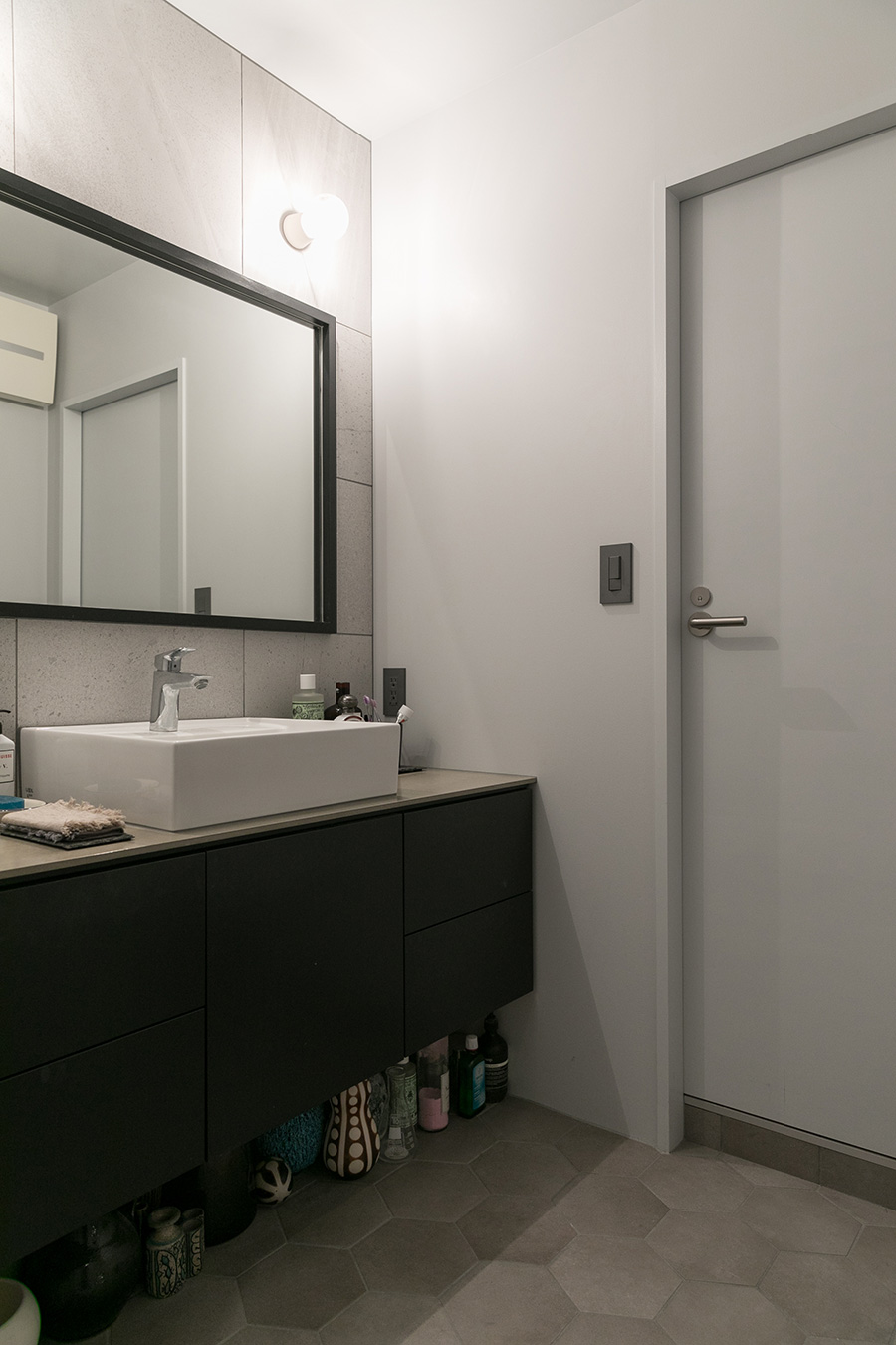 大きめのタイルを張った壁と、黒の縁の鏡がシックな洗面所。