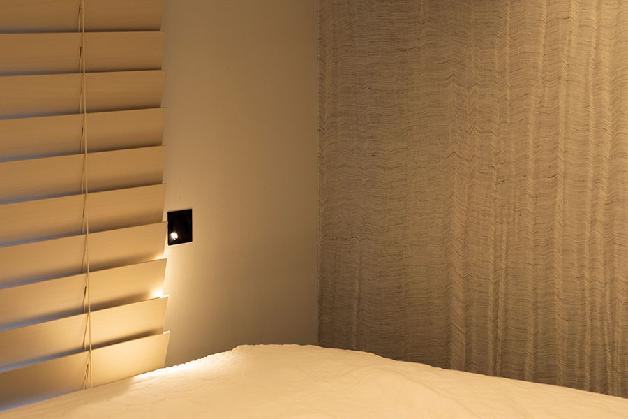 ベッドヘッドには、ホテルなどでも使用されるマイクロリーディングライトを左右対称に。一面だけ使った布クロスに光が反射して美しい。