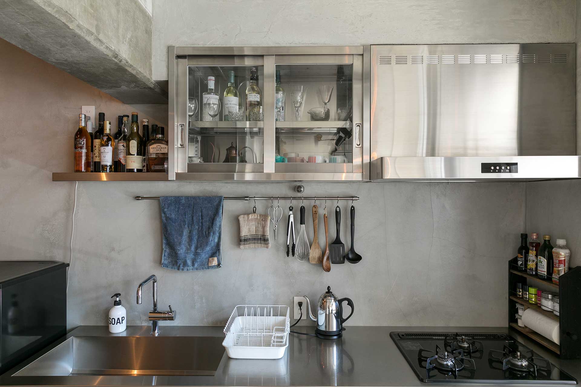ステンレスのシステムキッチンとモルタル壁のインダストリアルなキッチンスペース。