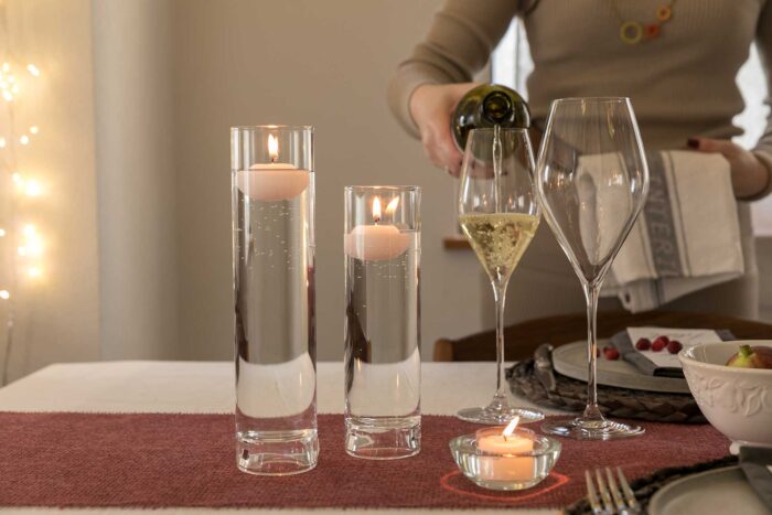 フローティングキャンドルとワイングラスの高低差を楽しむ。この耐熱ガラスのキャンドルホルダーは、上下を逆にして上にティーライトを置き、筒の中に松ぼっくりなどを入れて飾ってもいい。