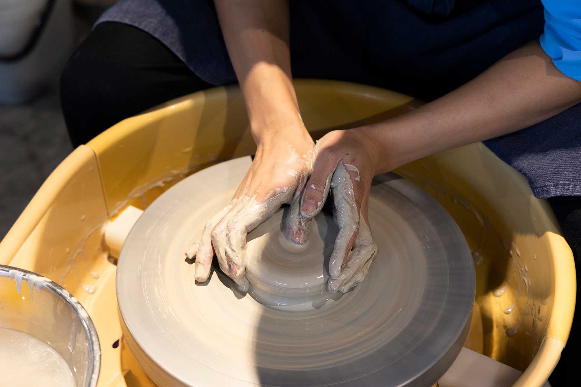 器の形を作っていく。両手で土をそっと包み込み、右手の親指を円の中心に移動させ、指先を下に倒して押し、下から１cmくらいのところまで穴を開ける。