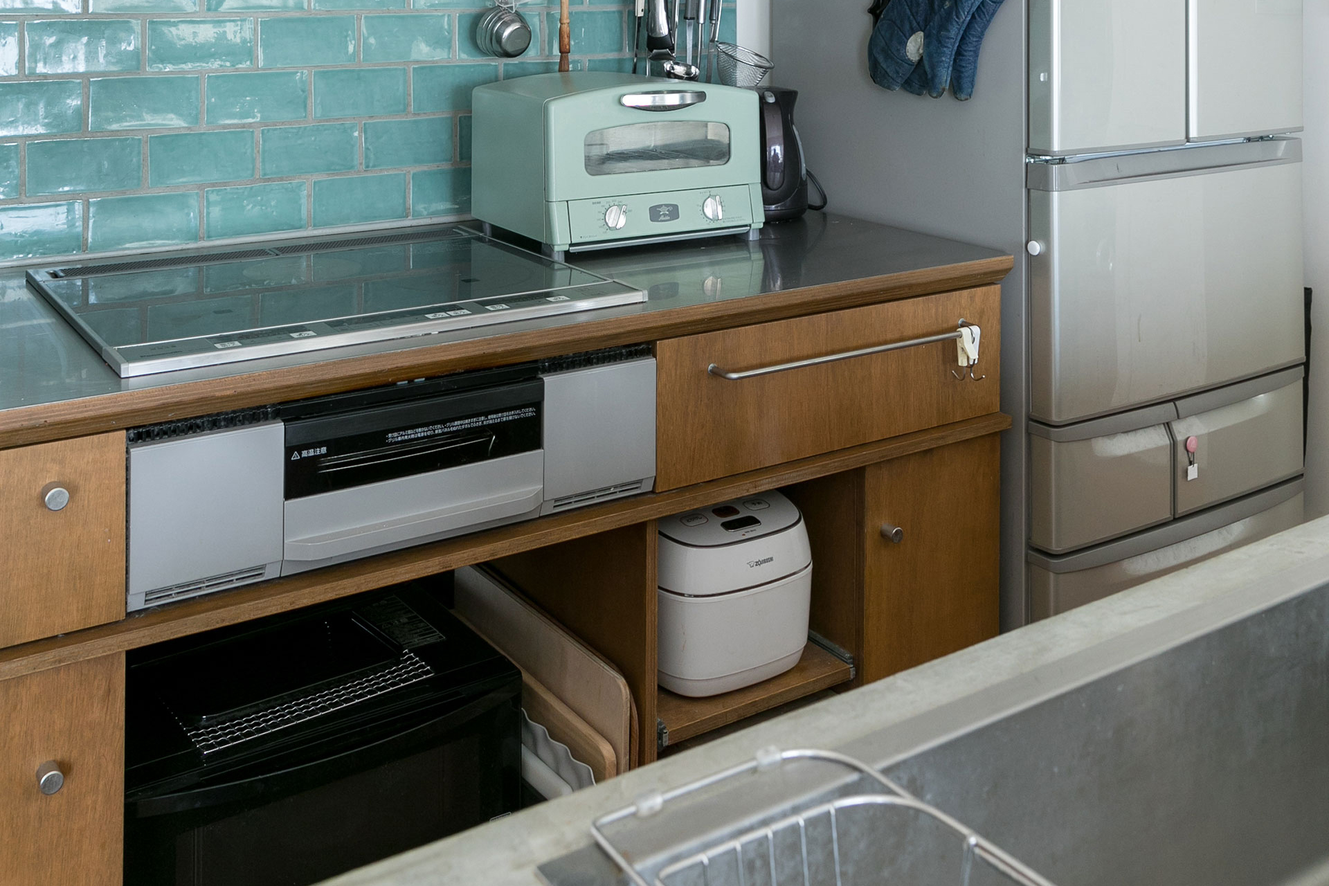 収納面にも配慮し、手持ちのキッチン家電がすっきり収まる。コンロ周りのタイルは、奥さまが好きなモスグリーンに。