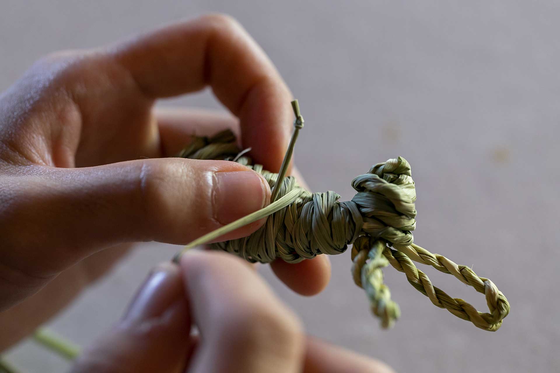 藁を固結びし、手を作る。くるっと巻いて藁の下を通す。同様に２箇所固結びを作り、脚を作る。