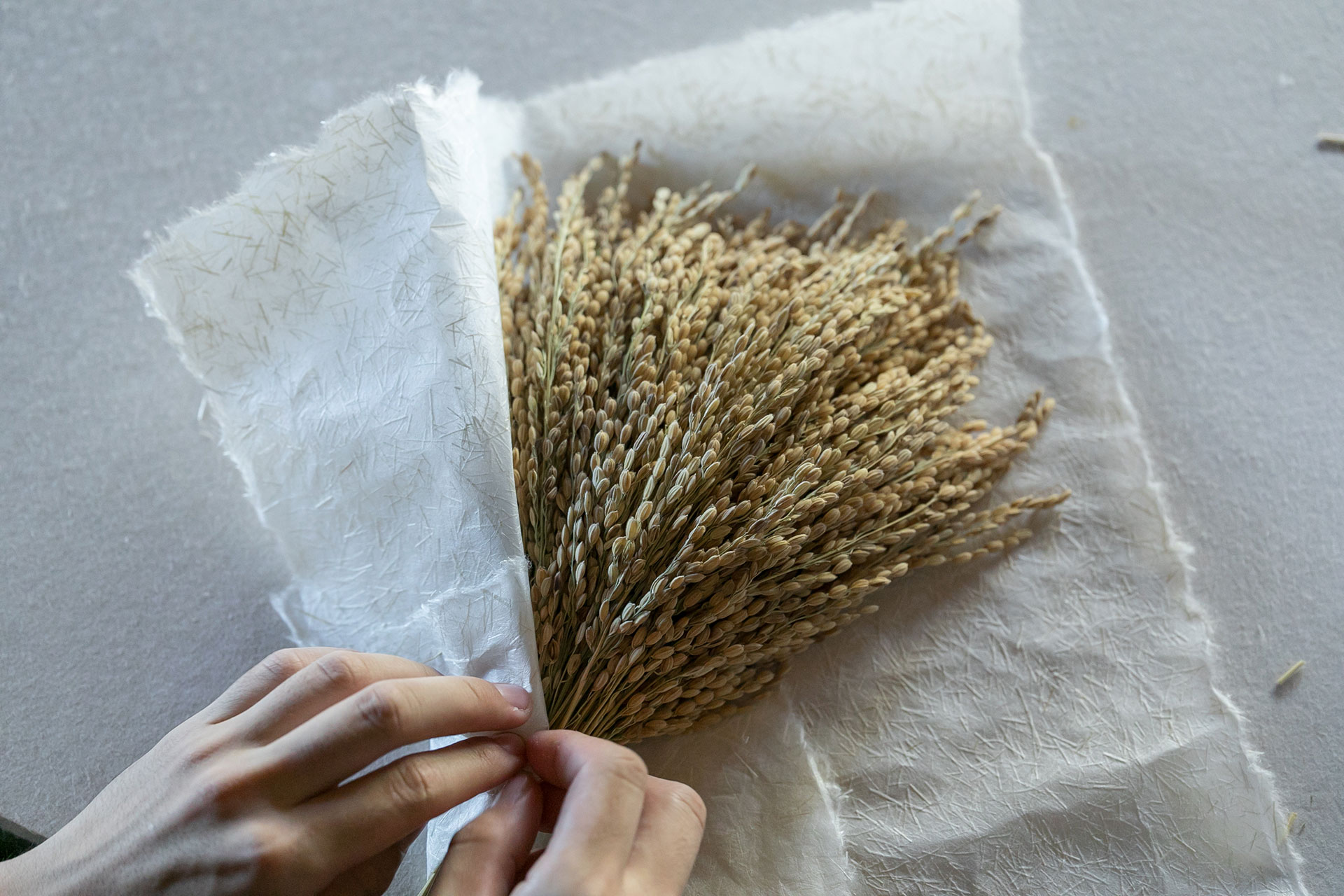 和紙に稲わらを斜めに置き、和紙を折りたたみながら稲わらを包み、末広がりの形を作る。