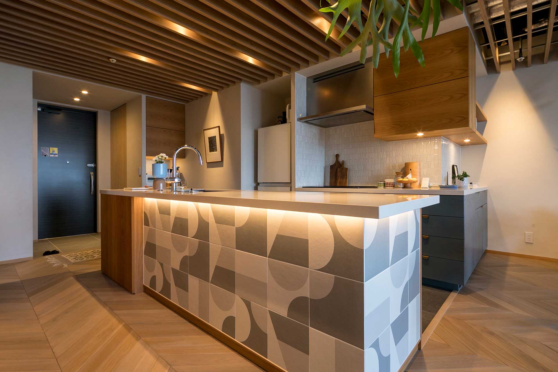 キッチンのパズル型のデザインのタイルが素敵。天板はサイルストーン。天板の裏にタイルを引き立たせる照明を仕込んでいる。タイルと木のバランスが美しい。