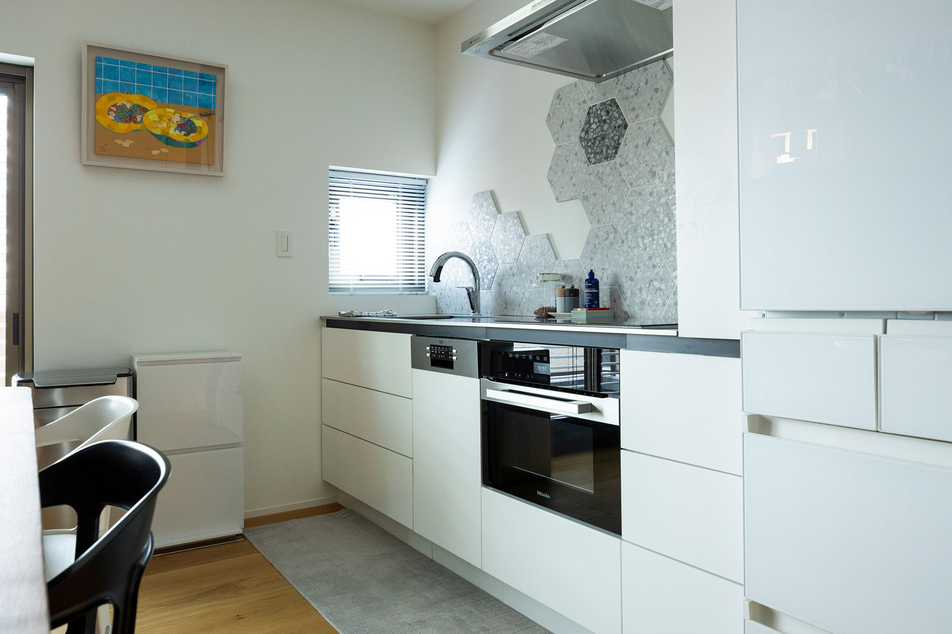 白をテーマにしたキッチン側。Mieleのコンロとオーブン、AEGの食洗機を指定して造作した。薄めの天板を少し浮かせることで軽やかに見せるなど、デザインを細かく指定した。キッチンにぴったりのアートは毛利美穂。