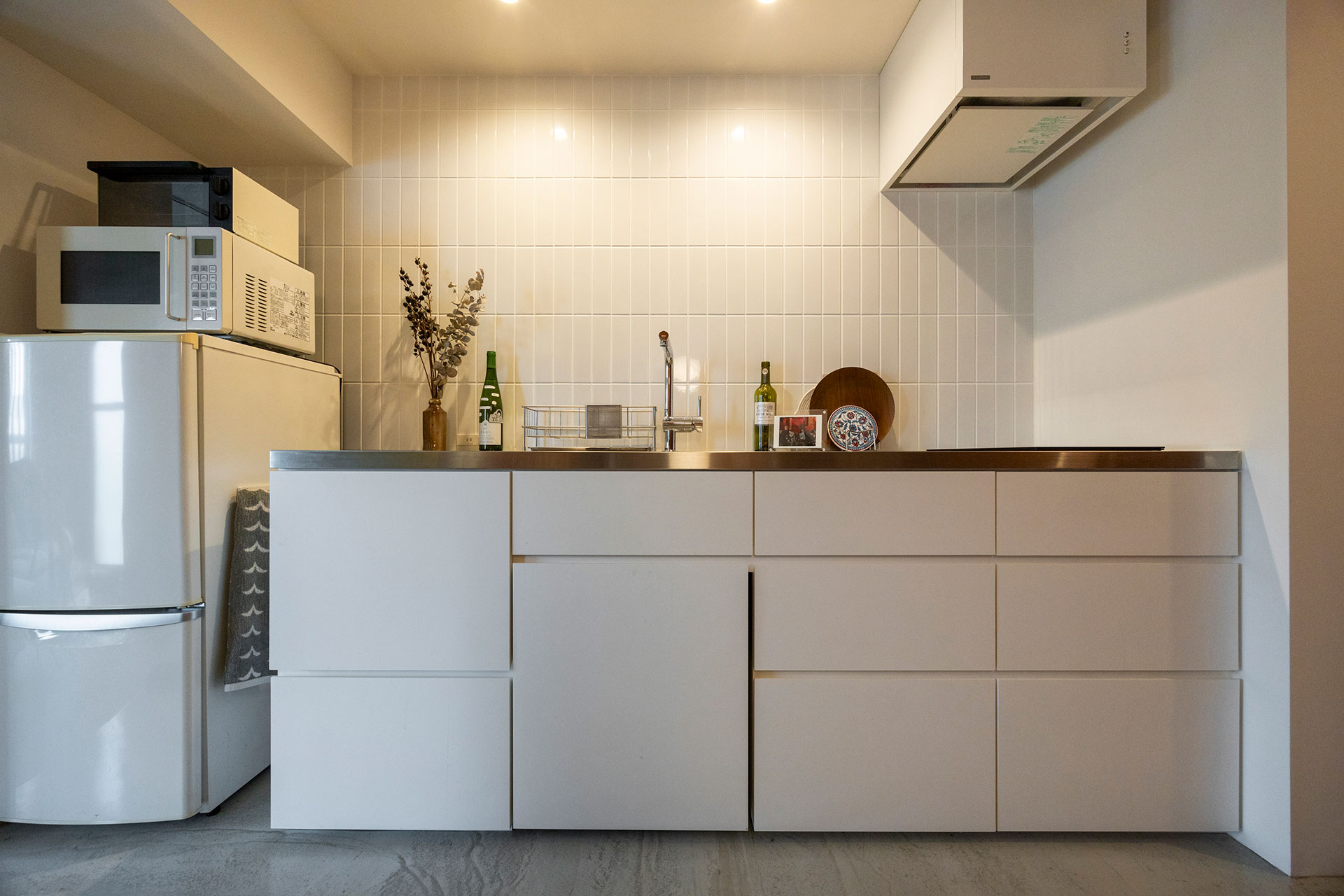 白で統一したキッチン。コンロは2口のIHにしてプレーンに見せるなど、シンプルなデザインにこだわった。ステンレスの天板の厚みもタイルの横幅とリンクしている。