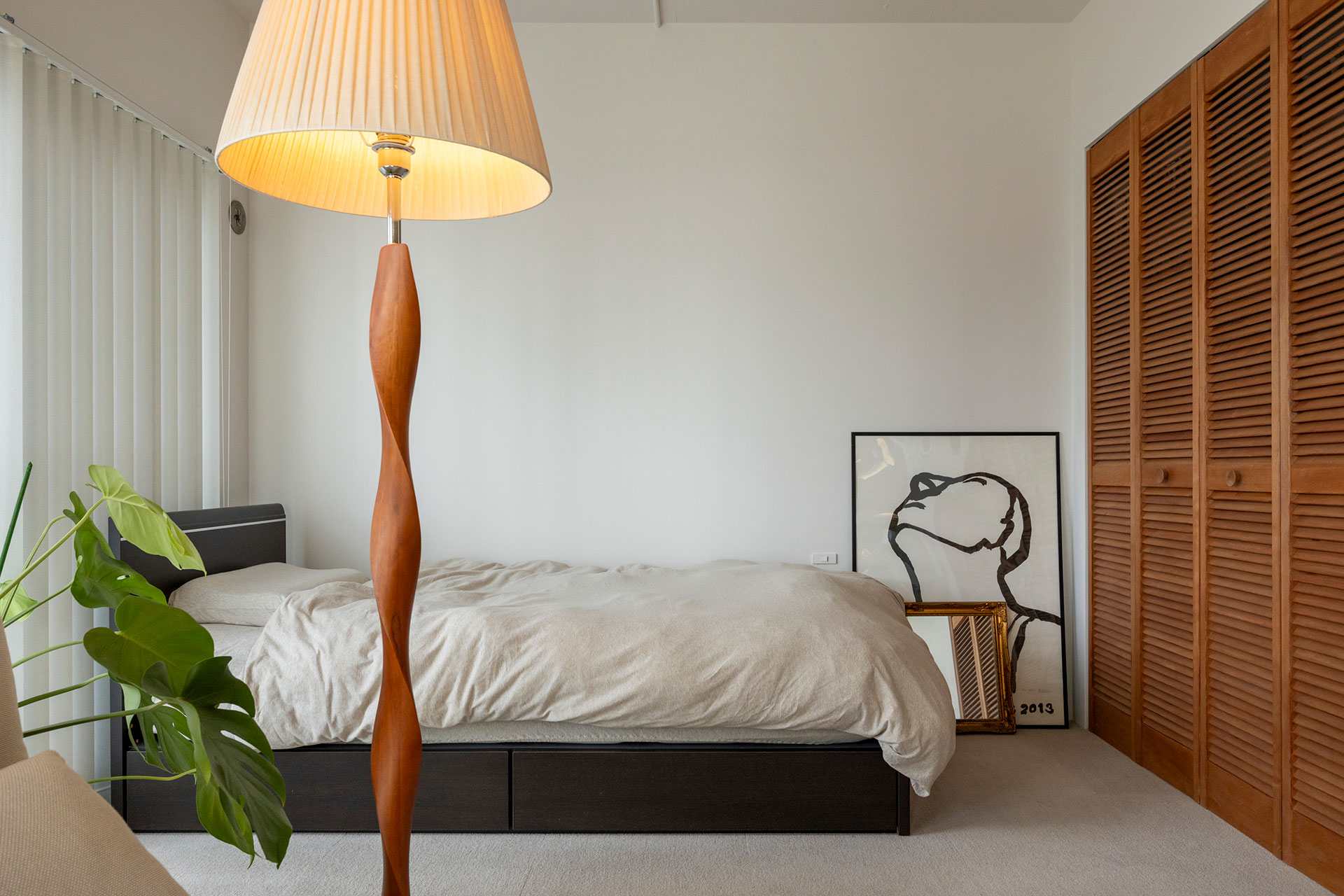 リビングの一角をベッドスペースに。本や掃除機、加湿器などを収めた収納にはルーバーの扉を取り付け、ダイニングのラワンに合わせて塗装した。フロアライトはネットで購入したノーブランドのもの。