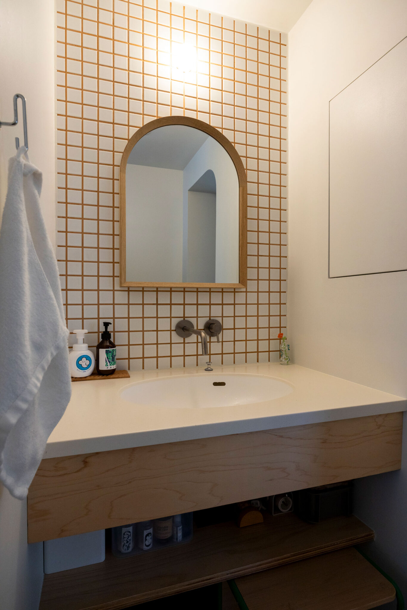 洗面の壁は、キッチンと反対色になるようタイルと目地をあしらった。R型の鏡がかわいい。