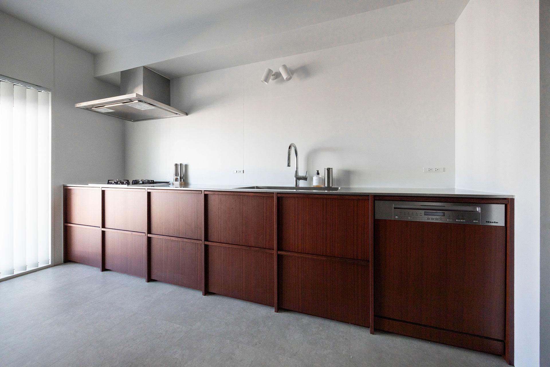 リブのデザインを施した造作キッチン。たくさんのサンプルの中からサペリマホガニーに決定。塩化ビタイルの床は、キッチンに合わせて暖色系グレーに。