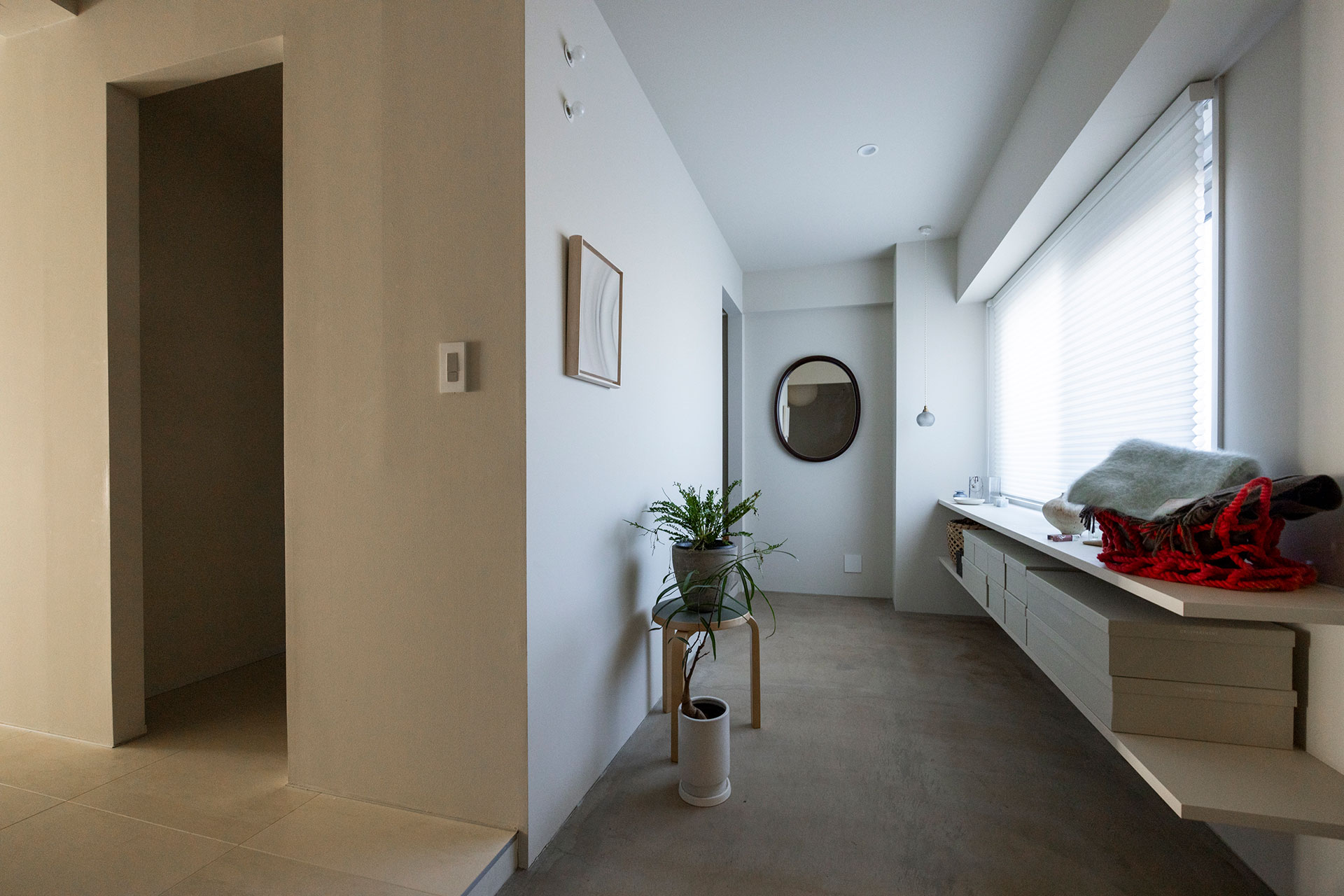 玄関脇にモルタルの土間が広がる。靴を収めるためのD&Departmentの収納ボックスがぴったり入るよう棚を造作してすっきりと。柳宗理デザインの曲木鏡の横から、左手のWTCへと続く。