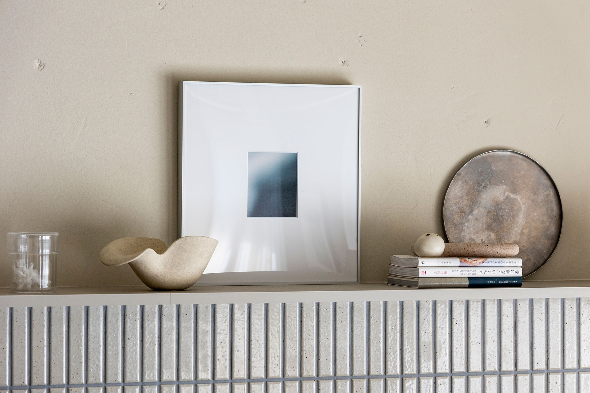 シルバーのトレーや陶器のシェード、ガラスのコップなど、素材の異なるものをミックスして飾る。額装しているのは、写真家・尾原深水の作品。