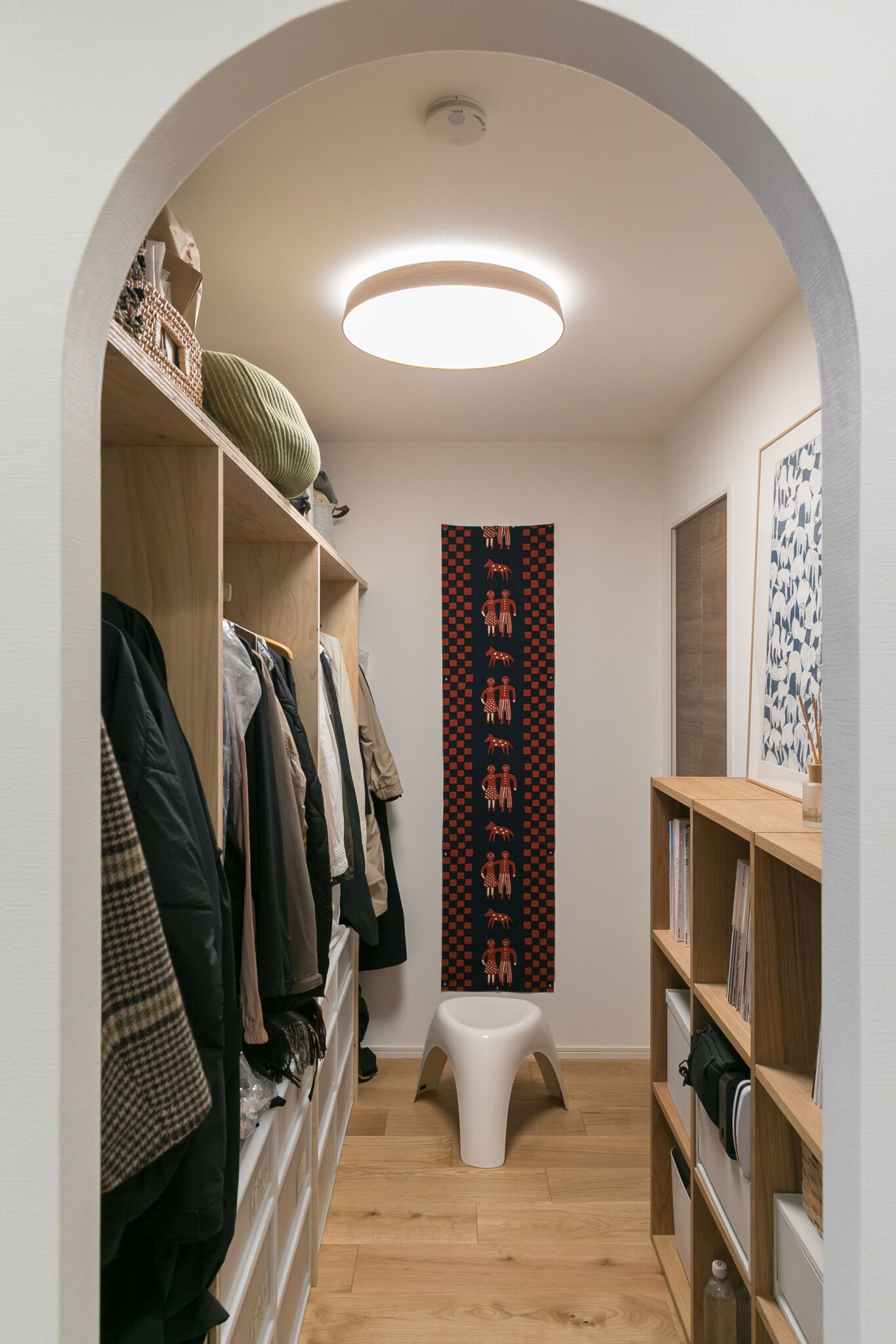 リビングからアーチをくぐるウォークインクローゼット。服の収納だけでなく、食料品を保管するパントリーを兼ねる。正面の壁には柚木沙弥郎のファブリックをタペストリーのように飾った。