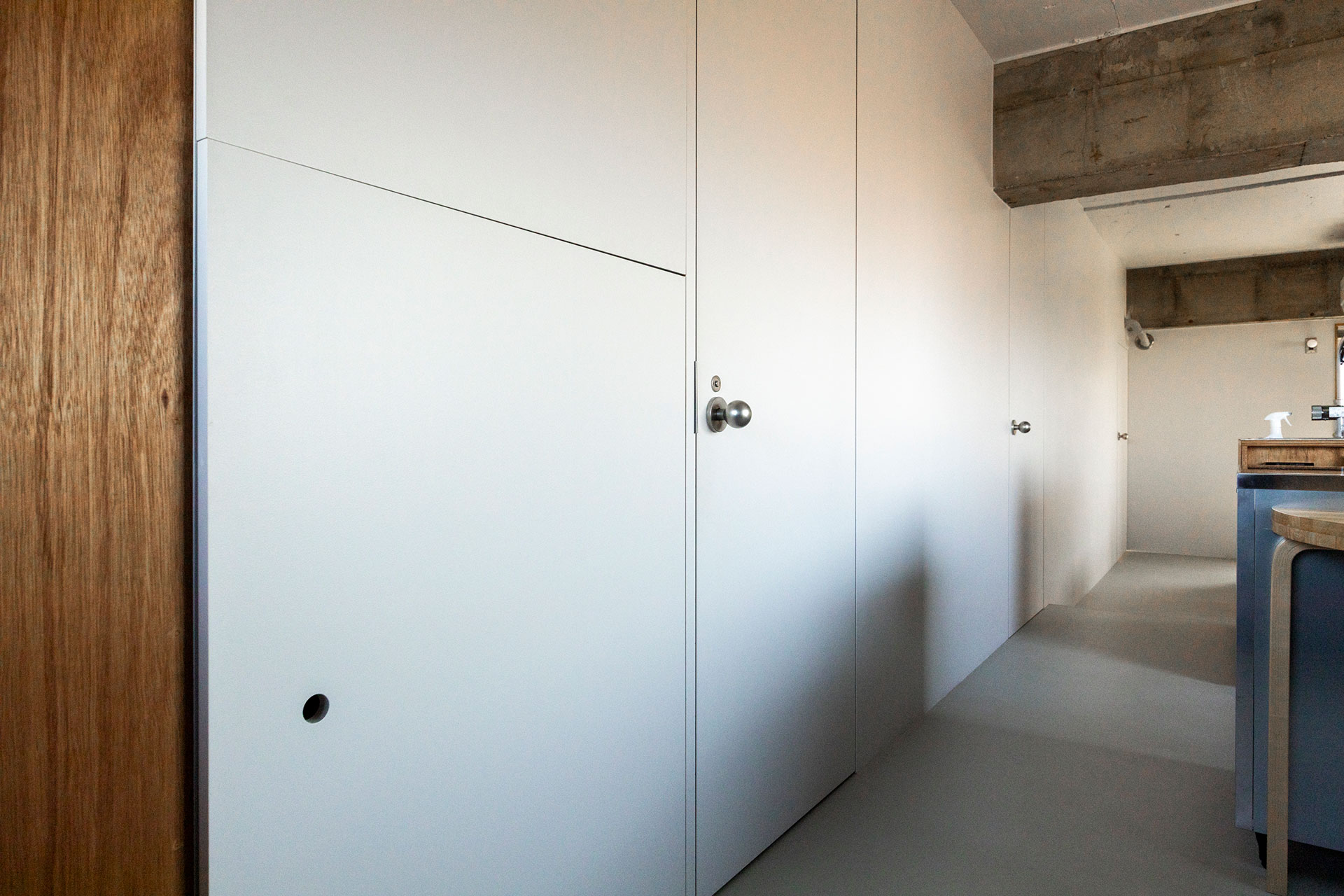 生活インフラスペースへのドアが並ぶ一面は、壁のよう。“握り玉”のドアノブは、受注生産の工業的な塗装を選択。