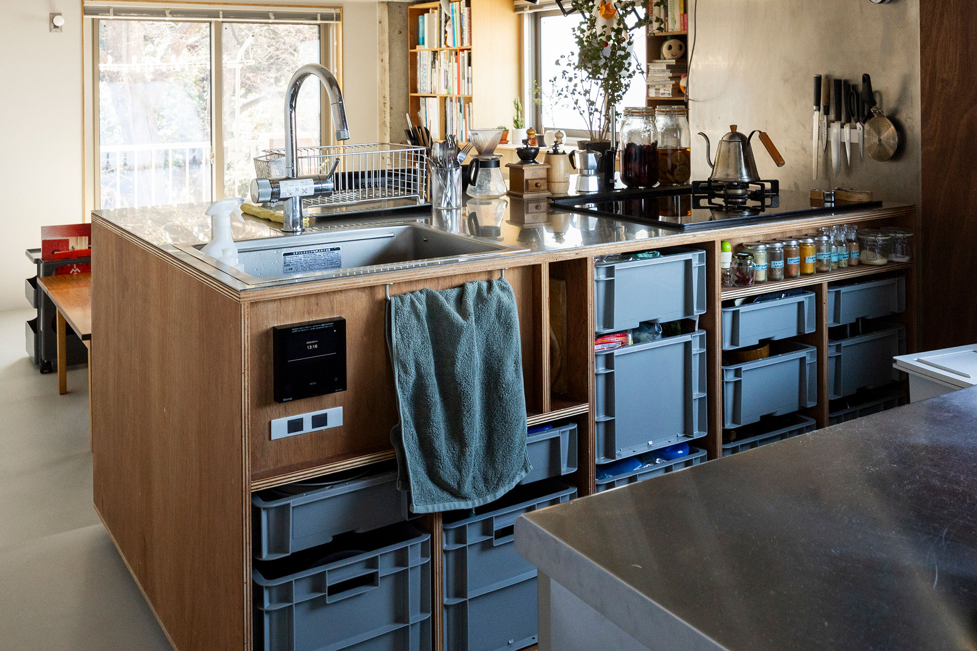 サンコーの業務用コンテナをLアングルで支えて引き出しに。調理器具、食器、食材などはキッチン側に収める。シンク下のスペースを活かして、スイッチパネル、給湯器リモコンを設置した。