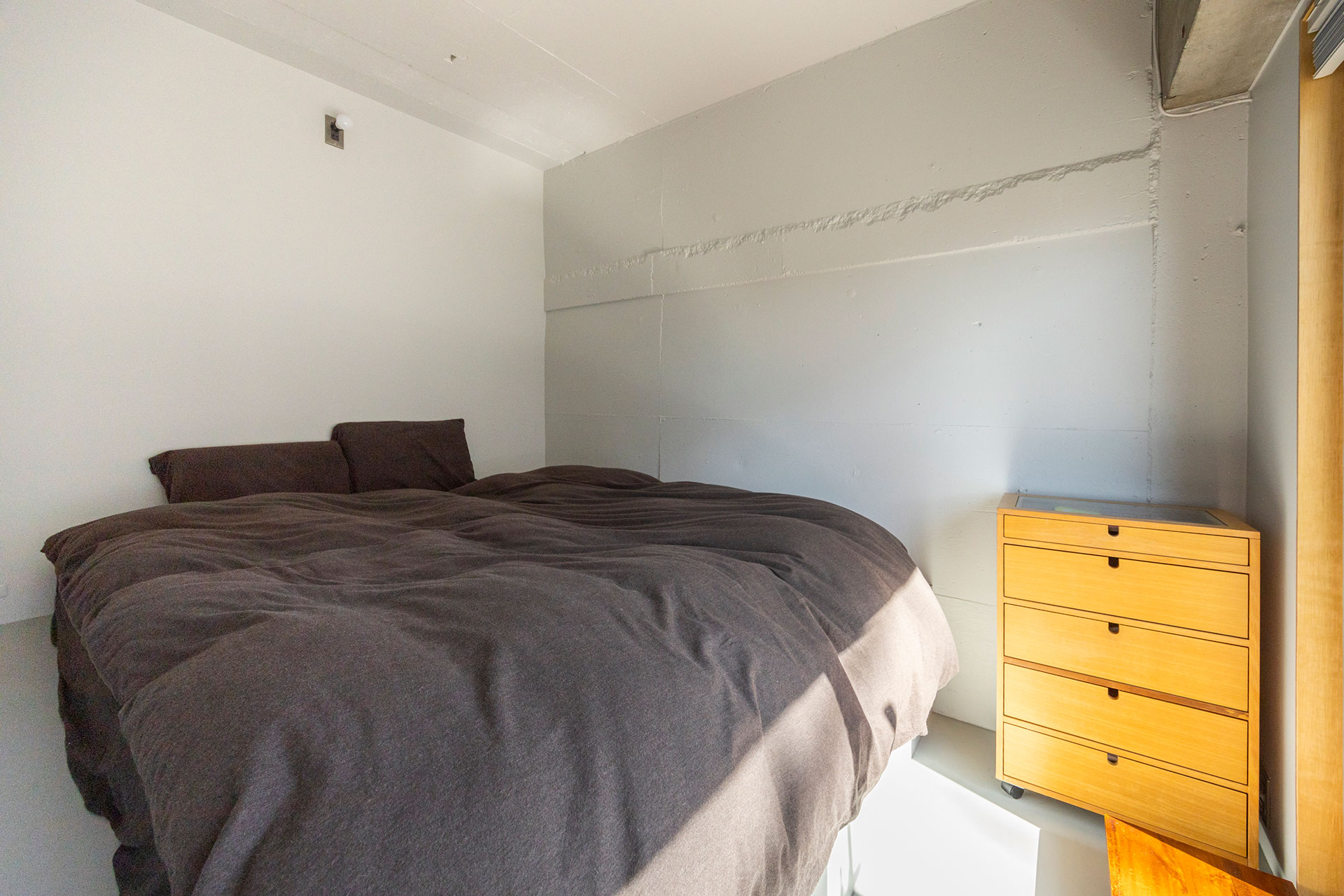 小上がりの上にマットレスを敷いたベッドルーム。ベッドの両サイドにコンセントやスイッチをシンメトリーに設置している。マットレスを外すと観音式の扉があり、小上がり収納が現れる。