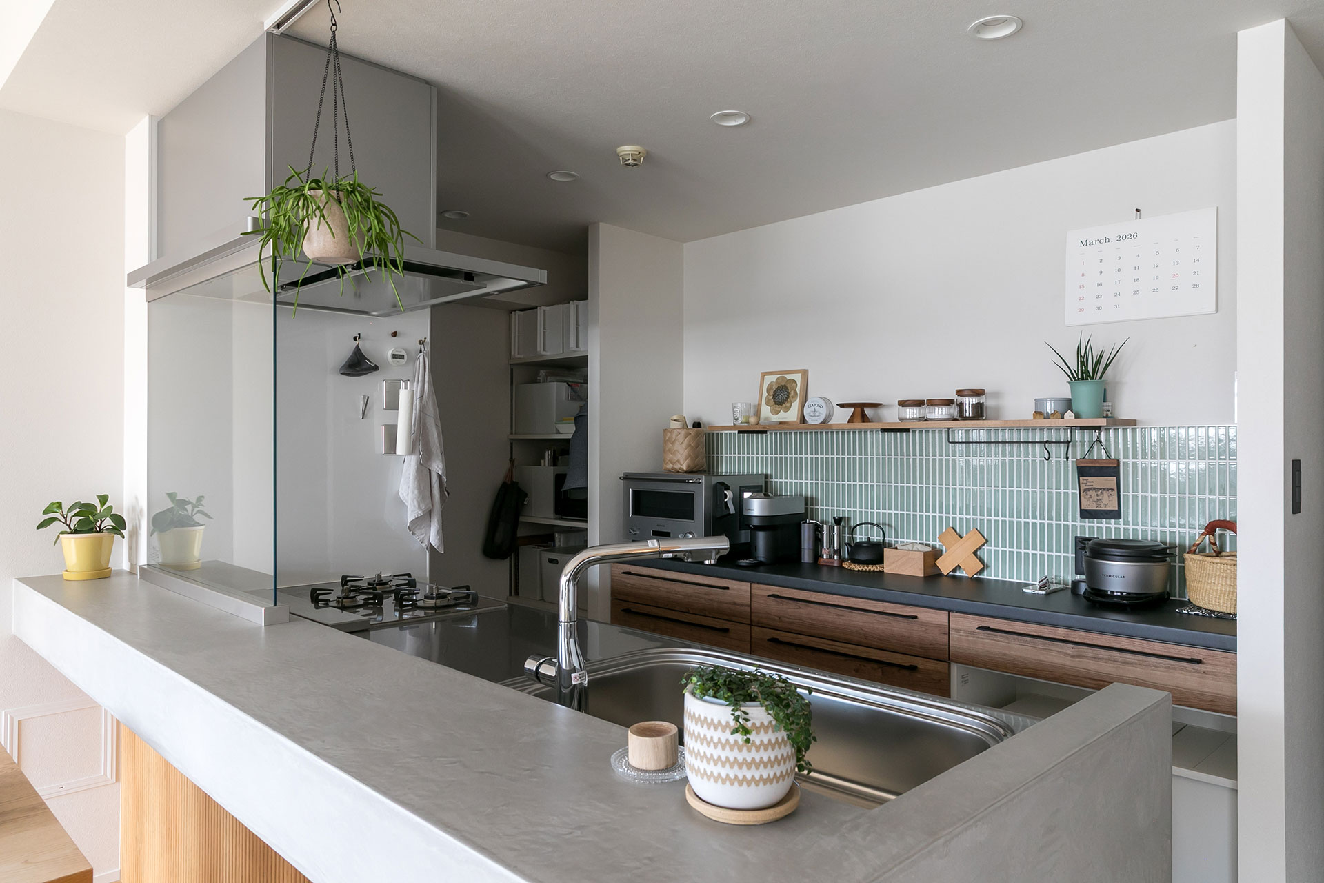 モラートで造作したキッチンカウンターに、背面の壁の緑のタイルが彩りを添える。オープンシェルフはあえて詰め込みすぎず、余白が心地よいリズムを生み出している。